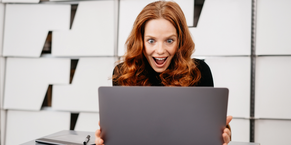 Rothaarige Frau sitzt vor Laptop und freut sich über Gebrauchtsoftware Angebote