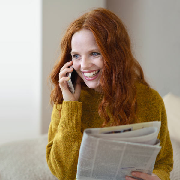 Frau hält eine Zeitung in der Hand und telefoniert